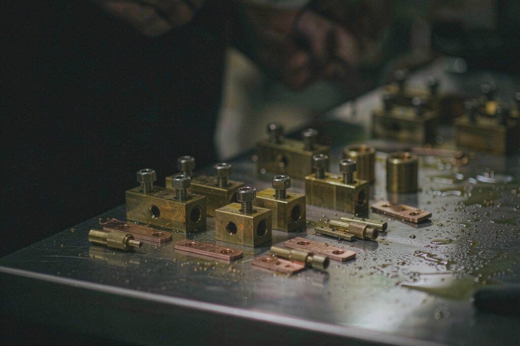Machined brass terminal blocks with hex socket set screws beside flat copper busbar strips with drilled holes and small knurled brass contact pins