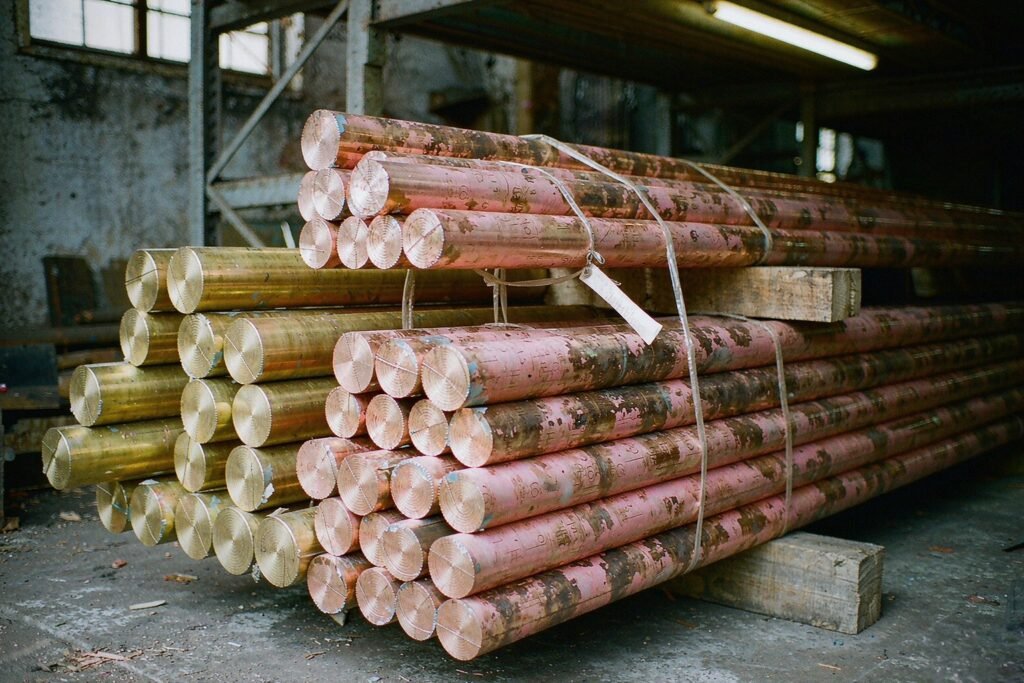 Bundles of brass and copper round bar in a warehouse rack, brass bars golden yellow and copper bars pink, with saw-cut ends, steel banding and wired paper tags