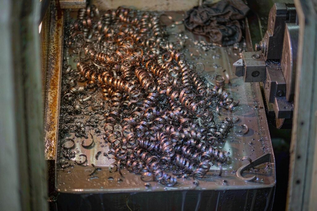 Long continuous steel turning chips tangled in the chip tray of a CNC lathe, temper colours from straw to blue, with the tool holder and carbide insert at the edge