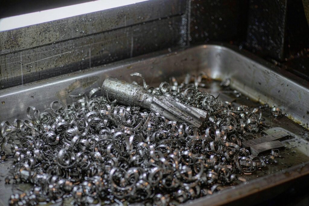 Curled titanium machining chips in a steel chip tray beside a worn carbide end mill, dark cutting-fluid residue on the tray