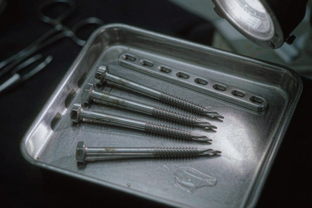 Titanium orthopaedic components on a steel tray: bone screws with threaded shafts and hex socket drives, and a straight bone plate with countersunk holes