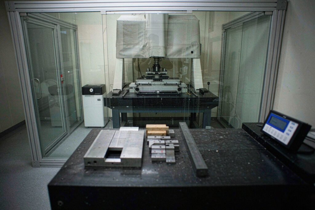 Machined aluminium and steel parts laid out in rows on a granite surface plate inside a temperature-controlled metrology room, soaking to room temperature before final inspection