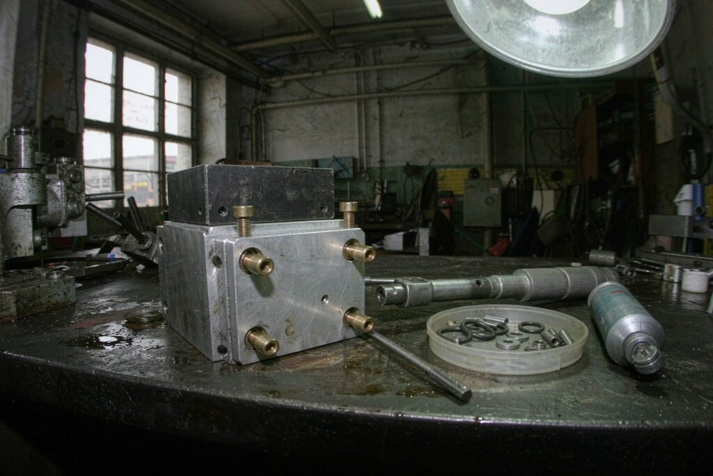 A mechanical assembly bench with a machined aluminium housing and its lid being fitted, four socket head screws part-tightened, a click-type torque wrench and a tray of O-rings, washers and dowel pins