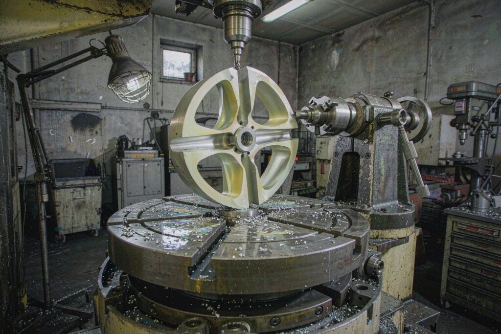 A five-axis trunnion table tilted at a compound angle holding a disc-shaped aluminium part with five curved blades, a ball-nose cutter working one blade inside the machine