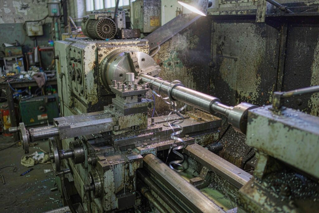A CNC lathe turning a stepped stainless steel shaft, a carbide insert cutting a shoulder while long stringy swarf coils away and cutting fluid runs down the shaft