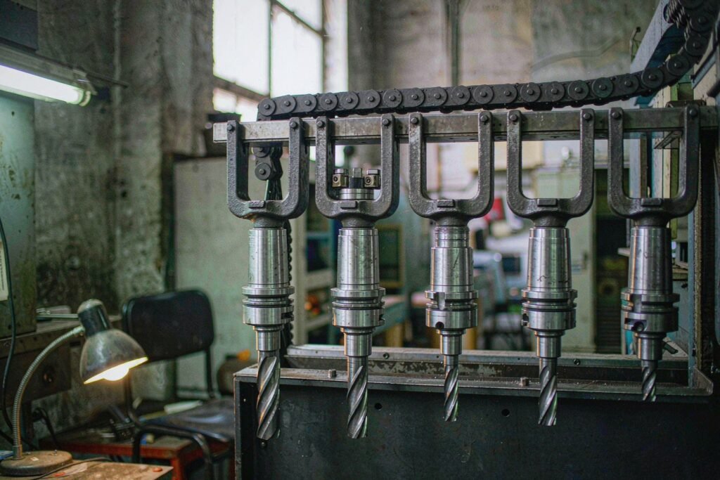 A CNC tool carousel magazine holding five toolholders of different lengths, a long end mill, an indexable face mill and a twist drill sitting in metal pocket forks