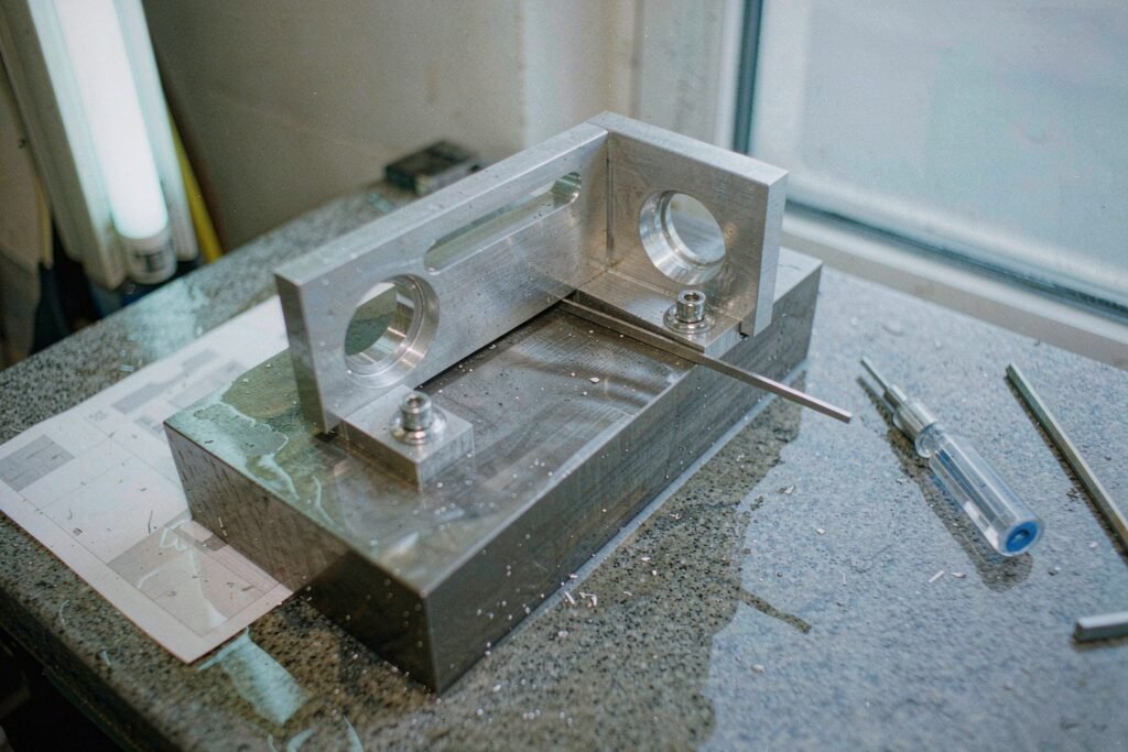 A prototype aluminium bracket test-fitted to a steel base block with two socket head cap screws, a feeler gauge blade in the joint gap and a torque screwdriver on a granite surface plate